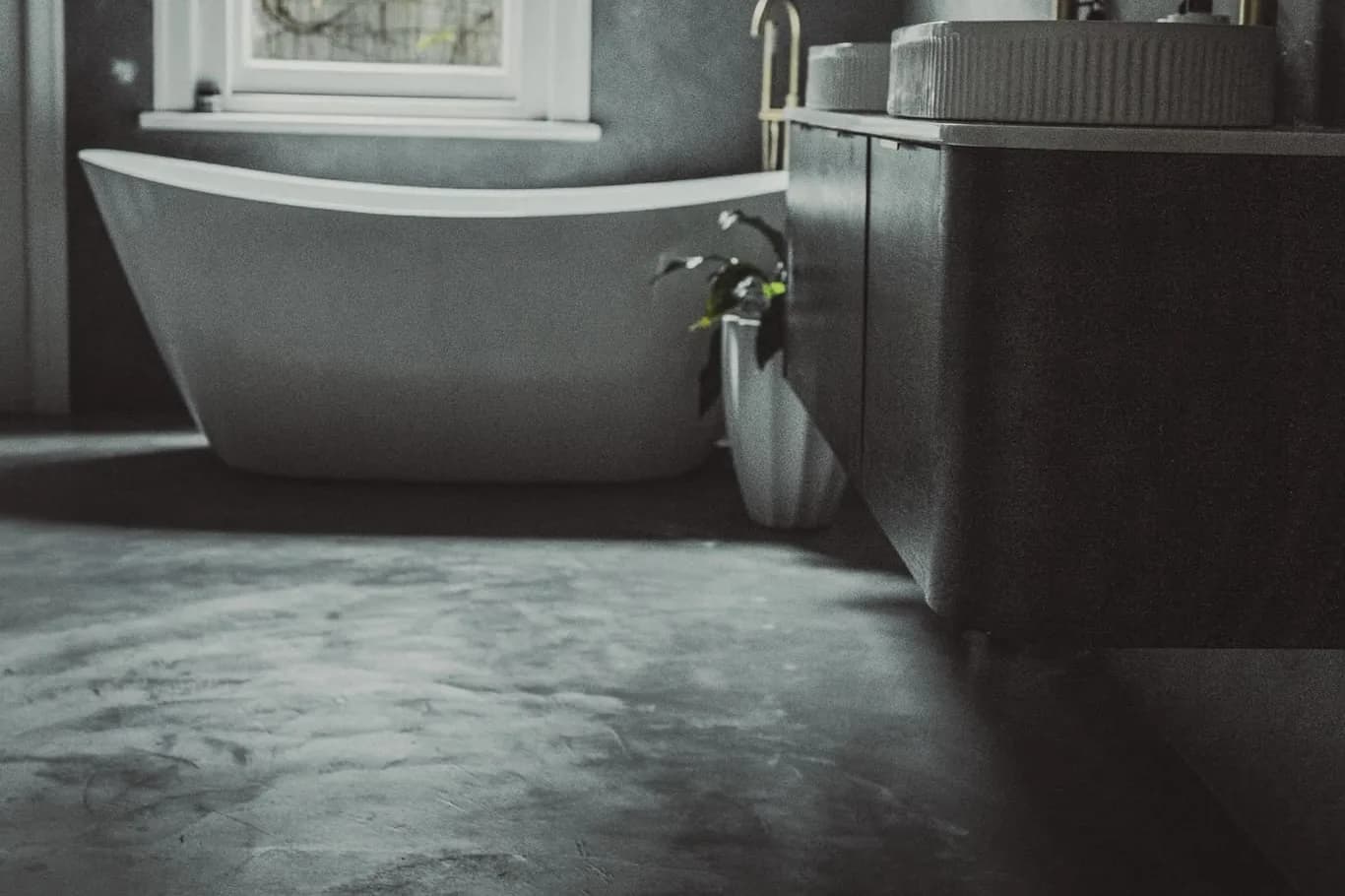 Bathroom with charcoal microcement walls and floor, a white freestanding bath and a dark vanity