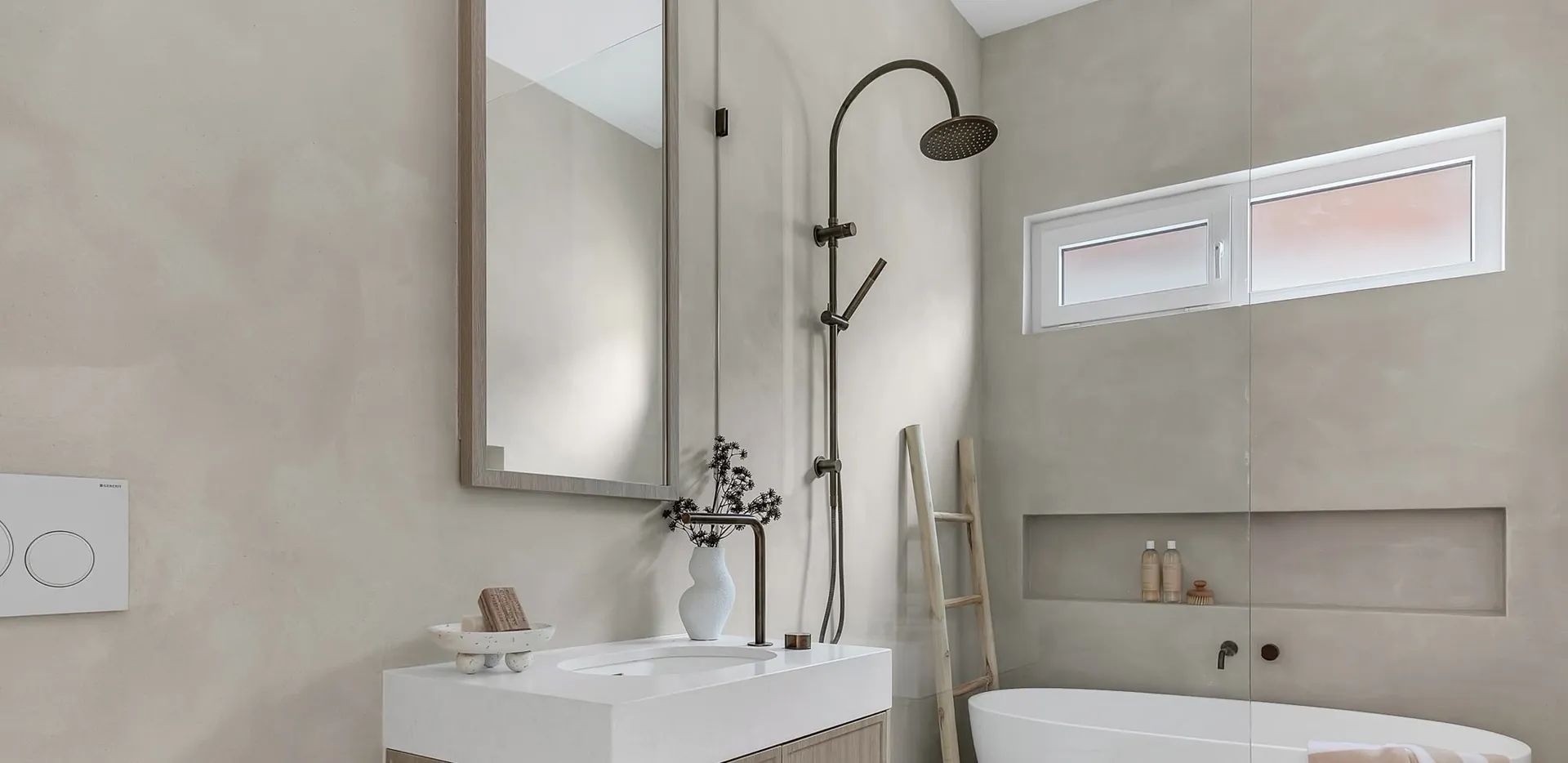Bathroom with pale microcement walls, a freestanding bath, a timber-look vanity and a black shower rail
