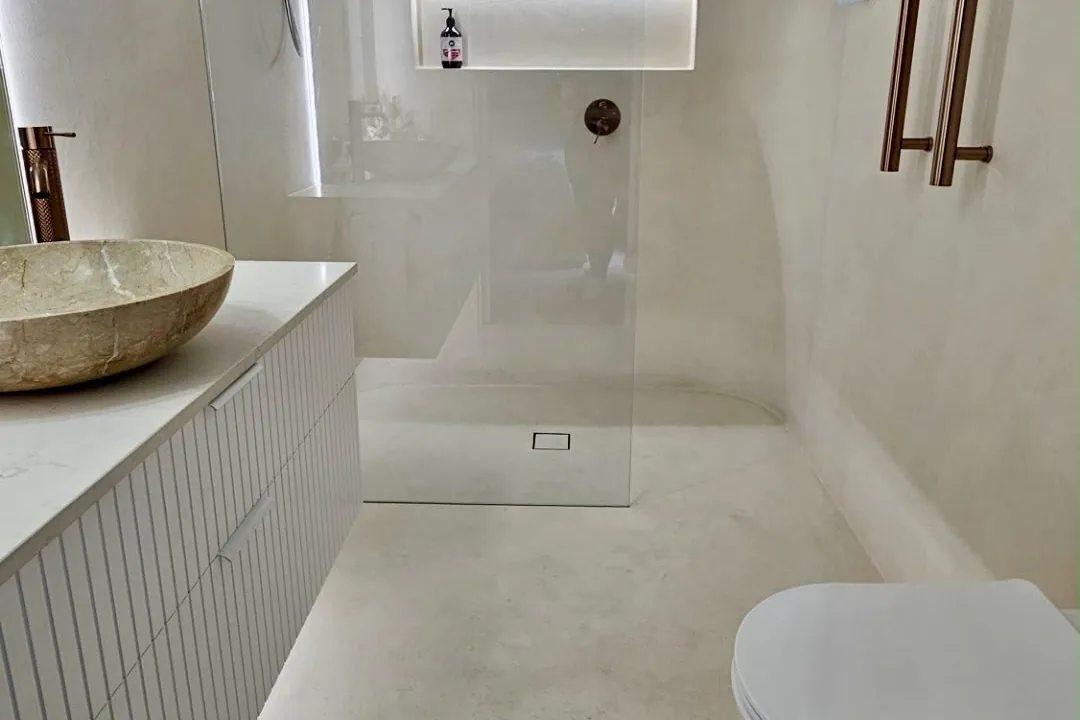 Bathroom with pale microcement walls and floor, a stone basin on a white vanity and a frameless shower screen
