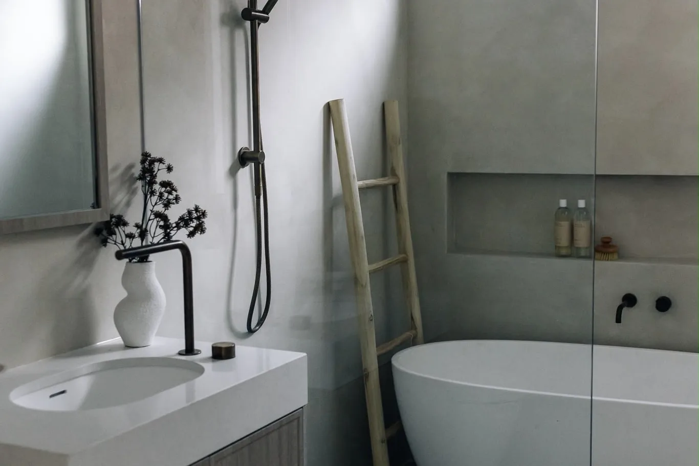 White basin, black tapware and a freestanding bath against pale microcement walls with a long recessed shelf