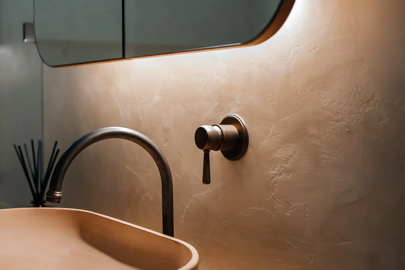 Bronze tap and mixer on a textured microcement wall above a basin